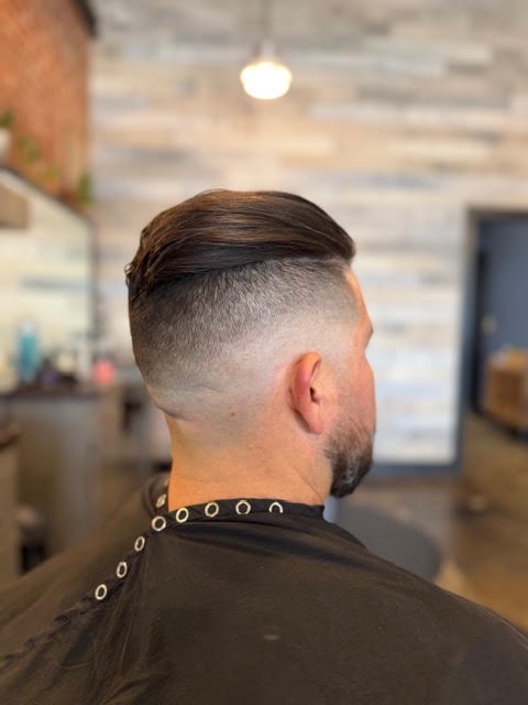 Men's low fade haircut with a slicked-back top, viewed from behind in the barbershop