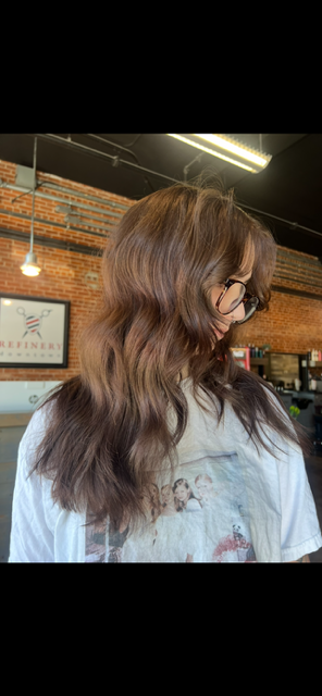 Woman with long layered brown waves styled in the salon against the exposed brick wall